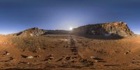 the image shows the sun behind a cliff in a mountainous area of dirt and mud