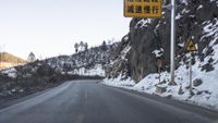 a sign is pointing left near a snowy road in an asian country area on a sunny day