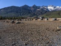 an open field with rocks and boulders surrounded by snowy peaks on a sunny day,