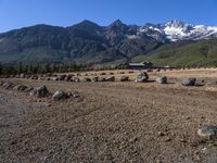 an open field with rocks and boulders surrounded by snowy peaks on a sunny day,