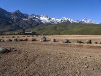 an open field with rocks and boulders surrounded by snowy peaks on a sunny day,