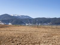 an empty field with some grass in it and mountains behind them in the distance with snow capped tops