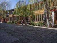 a sidewalk with a stone bench, trees and buildings and a person in the distance