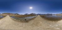 a fish eye lens shot of a pond with mountains in the back ground and sun shining on it