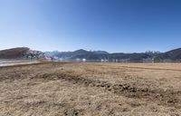 a sandy field with mountains in the distance in the background with a few snow capped mountains