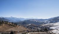 a large view of a valley with snow capped mountains in the distance with people on a bench