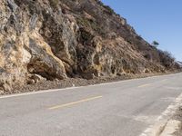 the motorcycle is traveling on the mountain road near the rocks and the hills, with no cars