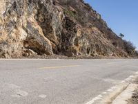 the motorcycle is traveling on the mountain road near the rocks and the hills, with no cars