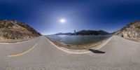 the sky is partly cloudy over a road and some water and rocks are under a sunny blue sky