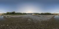 panorama photo taken from the reflection of a car in a puddle on a street next to water and trees