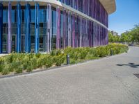 a building with pink glass and purple striped exterior is shown with the brick path on the left