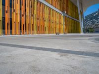 a concrete structure made into rows of orange and yellow poles are on a cement sidewalk