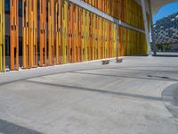 a concrete structure made into rows of orange and yellow poles are on a cement sidewalk