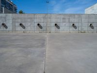 the empty parking lot in front of a wall with apartment buildings on it and a skateboarder on a ramp