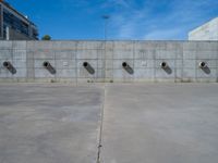 the empty parking lot in front of a wall with apartment buildings on it and a skateboarder on a ramp