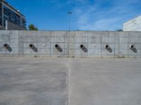 the empty parking lot in front of a wall with apartment buildings on it and a skateboarder on a ramp