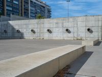 the empty parking lot in front of a wall with apartment buildings on it and a skateboarder on a ramp