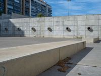 the empty parking lot in front of a wall with apartment buildings on it and a skateboarder on a ramp