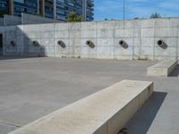 the empty parking lot in front of a wall with apartment buildings on it and a skateboarder on a ramp