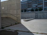 the empty parking lot in front of a wall with apartment buildings on it and a skateboarder on a ramp