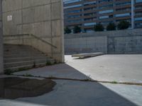 the empty parking lot in front of a wall with apartment buildings on it and a skateboarder on a ramp