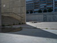 the empty parking lot in front of a wall with apartment buildings on it and a skateboarder on a ramp