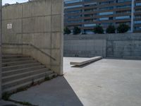 the empty parking lot in front of a wall with apartment buildings on it and a skateboarder on a ramp