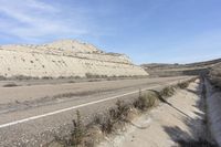 an old car drives down the road next to a rocky mountain side near a body of water