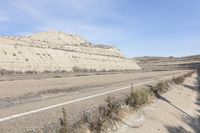 an old car drives down the road next to a rocky mountain side near a body of water