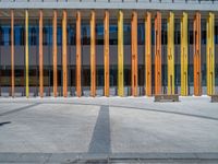 a concrete structure made into rows of orange and yellow poles are on a cement sidewalk