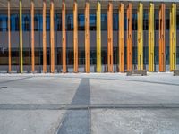 a concrete structure made into rows of orange and yellow poles are on a cement sidewalk