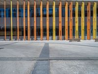 a concrete structure made into rows of orange and yellow poles are on a cement sidewalk