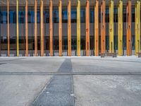 a concrete structure made into rows of orange and yellow poles are on a cement sidewalk