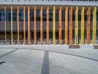 a concrete structure made into rows of orange and yellow poles are on a cement sidewalk