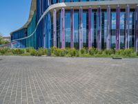 a building with pink glass and purple striped exterior is shown with the brick path on the left