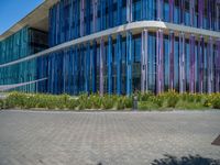 a building with pink glass and purple striped exterior is shown with the brick path on the left