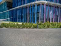 a building with pink glass and purple striped exterior is shown with the brick path on the left