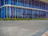 a building with pink glass and purple striped exterior is shown with the brick path on the left