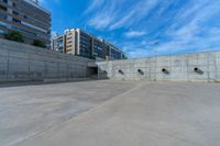 the empty parking lot in front of a wall with apartment buildings on it and a skateboarder on a ramp