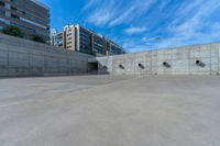 the empty parking lot in front of a wall with apartment buildings on it and a skateboarder on a ramp