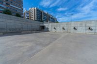 the empty parking lot in front of a wall with apartment buildings on it and a skateboarder on a ramp