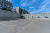 the empty parking lot in front of a wall with apartment buildings on it and a skateboarder on a ramp