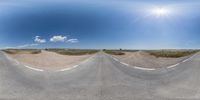 an empty road in the middle of some dunes with sun shining through the clouds overhead