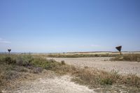 three signs are seen on the dirt and on the road side are some grass, and they are all by the land