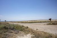 three signs are seen on the dirt and on the road side are some grass, and they are all by the land