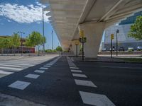 a car sitting at an empty street underneath a overpass overhang that contains a train stop, and cars and a pedestrian