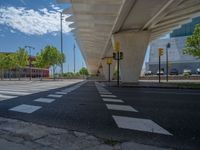 a car sitting at an empty street underneath a overpass overhang that contains a train stop, and cars and a pedestrian