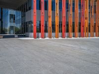 a concrete structure made into rows of orange and yellow poles are on a cement sidewalk