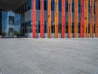 a concrete structure made into rows of orange and yellow poles are on a cement sidewalk