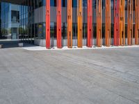 a concrete structure made into rows of orange and yellow poles are on a cement sidewalk